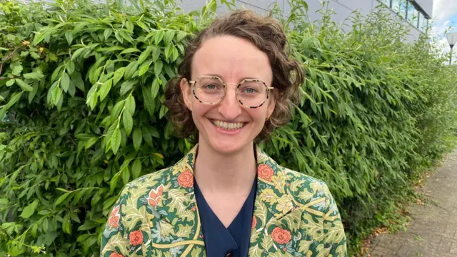 Green Party Candidate Kathryn Fisher smiling and looking directly at the camera, wearing a green foliage-patterned jacket.