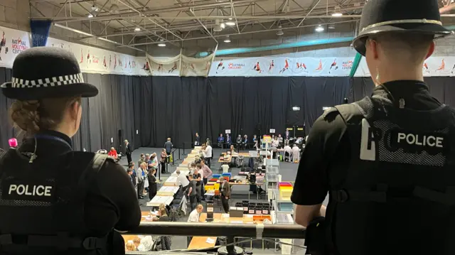 Two police officers standing on a balcony overlooking the counting tables at Kettering Leisure Village