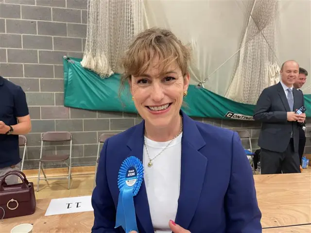 Victoria Atkins wearing a blue jacket, white top and Conservative rosette smiling