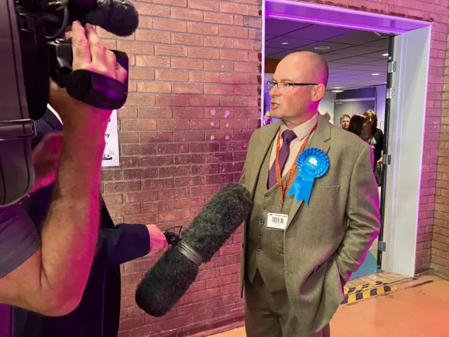 A man speaks to a reporter holding a large camera