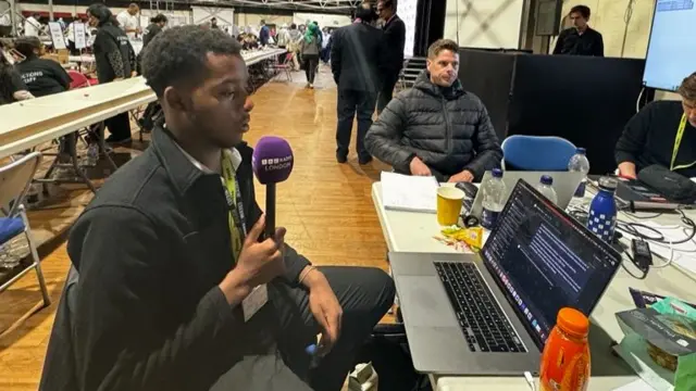 Reporter William Wandji sitting at press desk at Harrow count