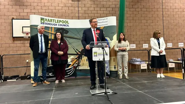 A man at a podium with candidates on stage