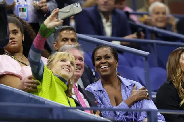 Former First Lady of the United States Michelle Obama poses for a selfie in the stands on Arthur Ashe Stadium at the US Open