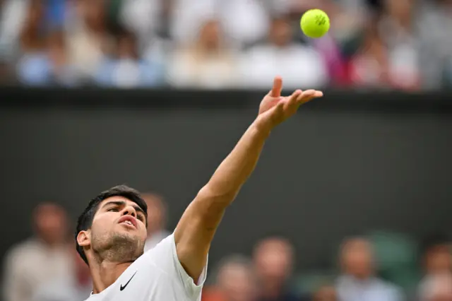 Carlos Alcaraz tosses the ball to serve wearing an all-white Nike top