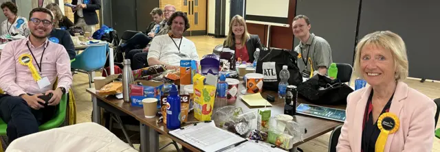 Lib Dems sat around a table full of snacks such as Jelly Babies and apple juice cartons