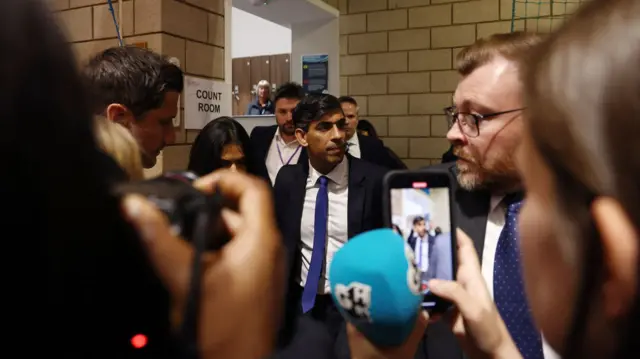 Rishi Sunak looking downbeat as he walks into building, with crowds of press in front taking pictures