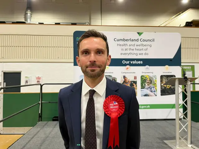 Labour candidate Josh McAlister winning a blue suit and red rossette