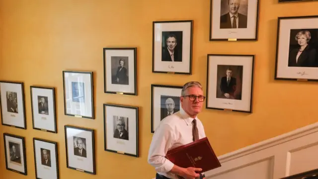 M Keir Starmer walking past portraits of previous UK Prime Ministers on the stairs inside Number Ten Downing Street