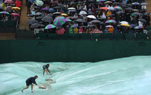 Fans huddle under umbrellas as Wimbledon groundstaff mop up water