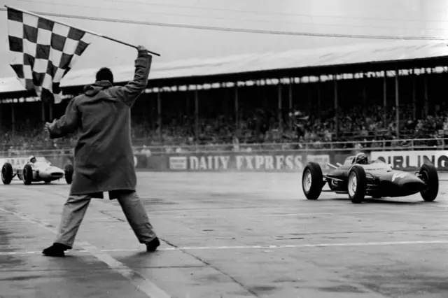 John Surtees crosses the line as the chequered flag is waved at the British Grand Prix in 1962