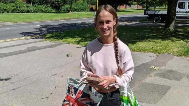 Jessica Ligh standing in the street smiling holding two shopping bags and her purse and wearing a jumper and jeans