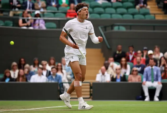 Ben Shelton holds a tennis racquet and pumps his fist in celebration