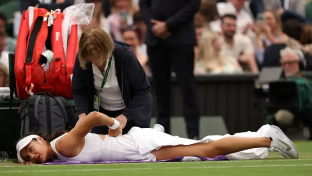 Emma Raducanu lies on the floor as she receives treatment