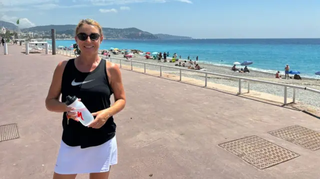 Céline on the coast of Nice with a blue sky and beach behind her