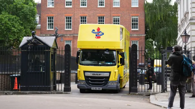 Bright yellow removal van for the company Bishop's Move drives through gates outside Downing Street