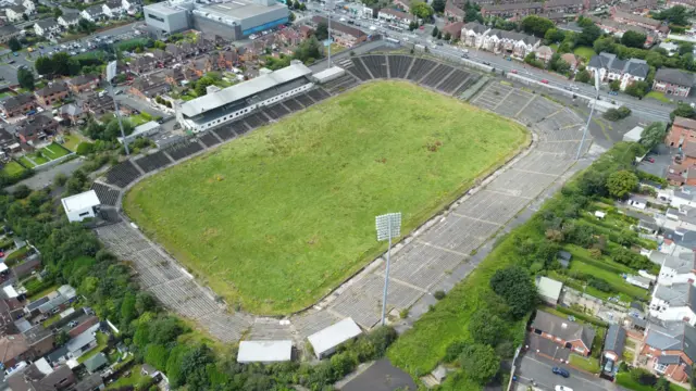 Casement Park as seen from above. Stadium sits in the middle of rows of houses. The terraced stands are derelict and grass overgrown in the middle