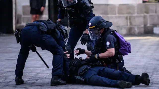 A riot police officer laying on the ground being tended to be colleagues