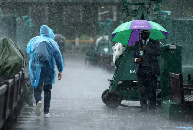 A fan wearing a poncho and a security guard under an umbrella