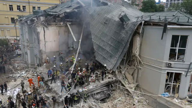 Rescue workers at the site of a strike at a children's hospital in Kyiv. The roof of the facility has caved in and there are plumes of smoke.