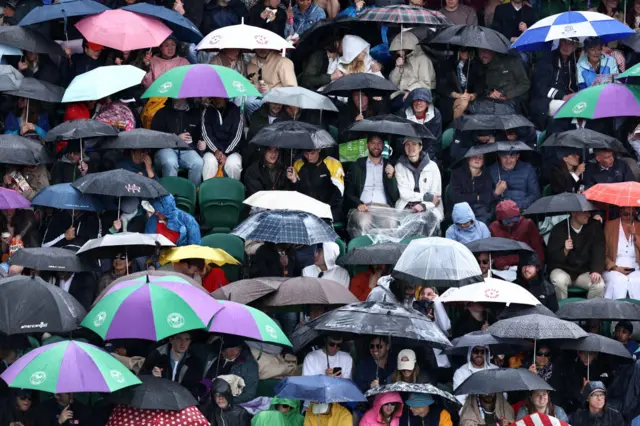 Fans sit under umbrellas at Wimbledon