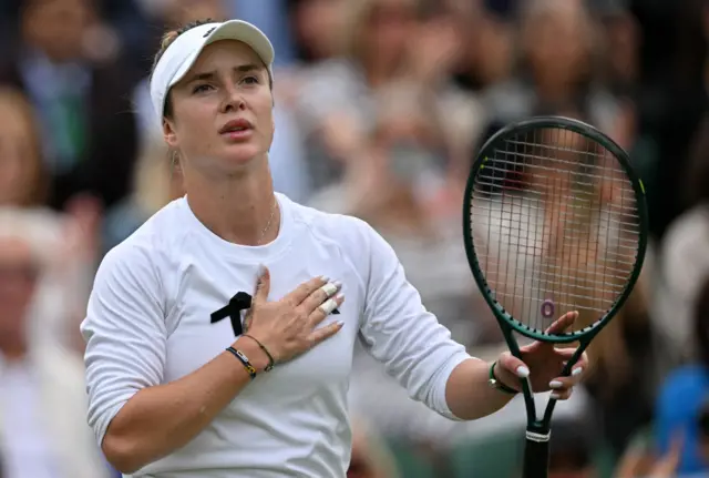 Elina Svitolina holds her hand to her chest and holds up a tennis racquet