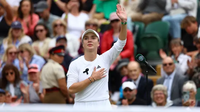 Ukrainian tennis player Elina Svitolina with one hand on her chest and the other raised up on a court.