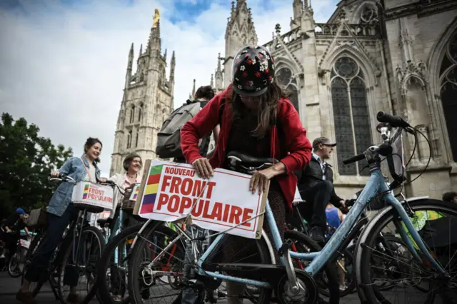 A woman affixes a sign saying Nouveau Front Populaire onto her bike in Bordeaux, France