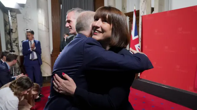 Rachel Reeves hugs Jonathan Reynolds in front of the backdrop to her speech