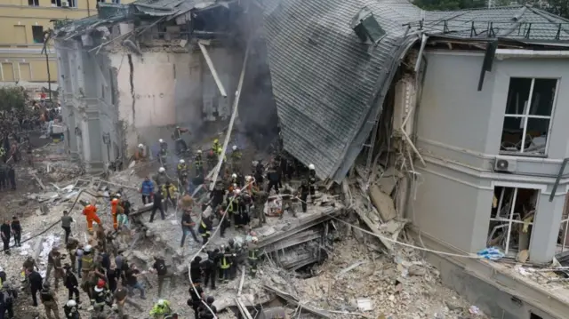 Rescue workers searching the rubble of a partially- destroyed hospital building, a large portion of the building has been levelled and in other areas the roof has fallen in