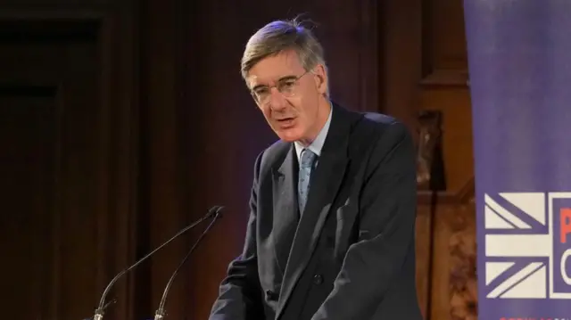 Jacob Rees-Mogg speaking into two microphones from a lectern