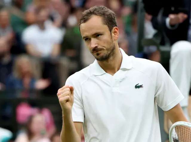 Daniil Medvedev clenches his fist in celebration wearing a white Lacoste polo shirt