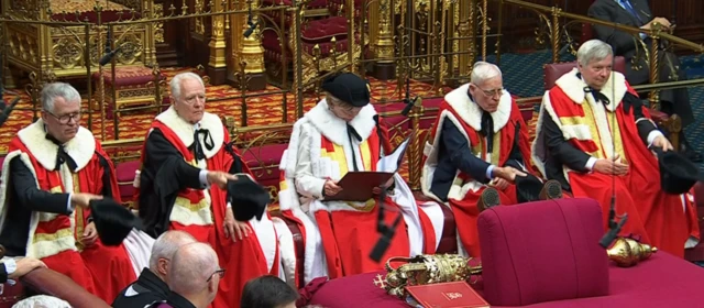 Five members of House of Lords in their formal ermine robes, removing their caps as part of the ceremony