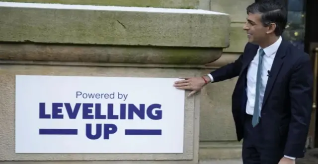 Rishi Sunak poses next to a levelling up sign