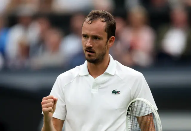 Daniil Medvedev clenches his fist in celebration wearing a white Lacoste polo shirt