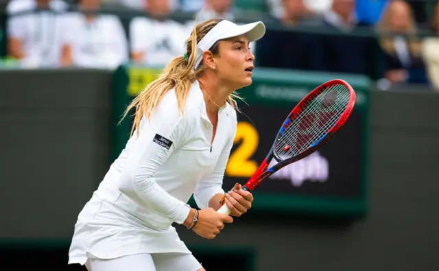 Donna Vekic on court wearing a full white outfit with a white visor