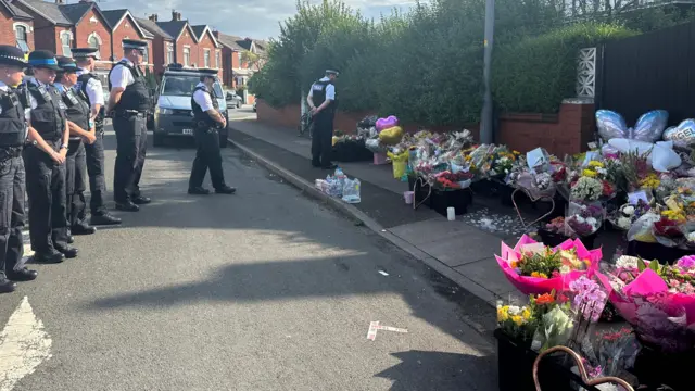 Police officers stand in a row in front of flowers laid on the pavement