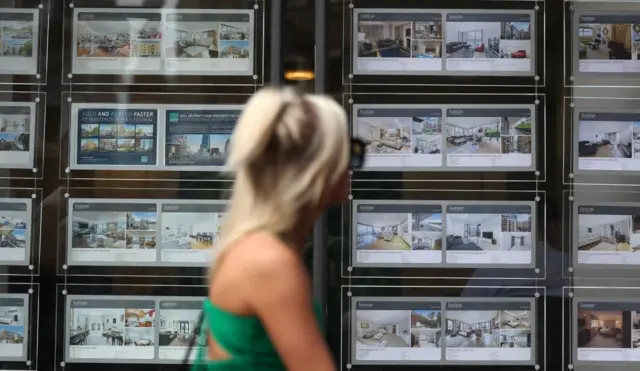 A pedestrian looks over real estate at an estate agent in London