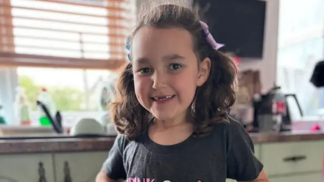 Bebe King has her hair in two pigtails and stands smiling at the camera