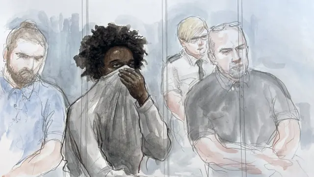 Rudakubana covers his face with a jumper behind glass in the dock