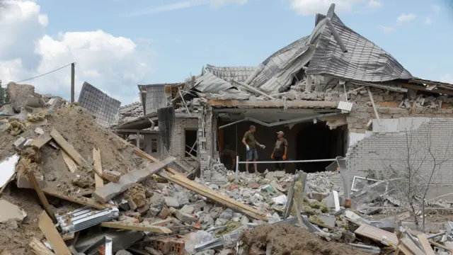 Two men stand in the structure of a building among debris