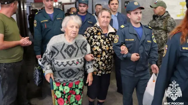 Two women walking alongside specialists from the Russian Emergencies Ministry