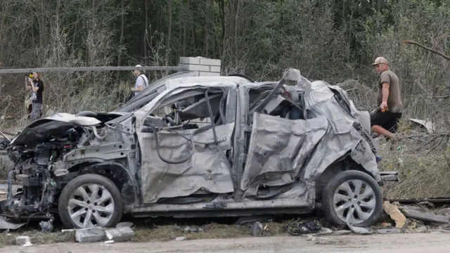 A destroyed car on the side of the road with people behind