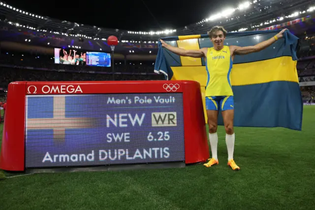 Mondo Duplantis with the Swedish flag in front of world record board