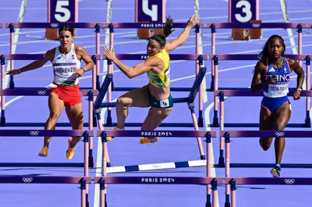 Australia's Michelle Jenneke falls as Hungary's Greta Kerekes (L) and France's Cyrena Samba-Mayela (R) compete in the women's 100m hurdles heat of the athletics event at the Paris 2024 Olympic Games at Stade de France in Saint-Denis