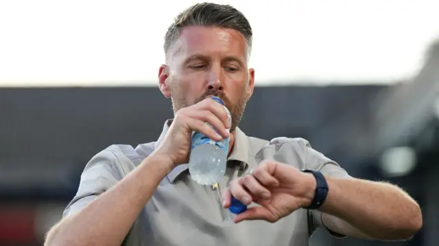 Luton boss Rob Edwards drinks a bottle of water while checking his watch