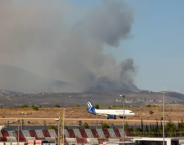 A plane on the runway with smoke billowing in the background