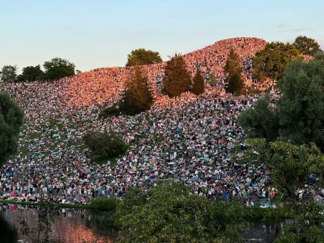 A huge crowd of people gather on a grassy hill nearby Swift’s Munich venue to listen to the show