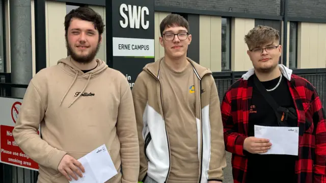 Students Kian Cassidy, Aleksander Zmuda, and Oliver Piech pose for the camera holding paper with their results written on it