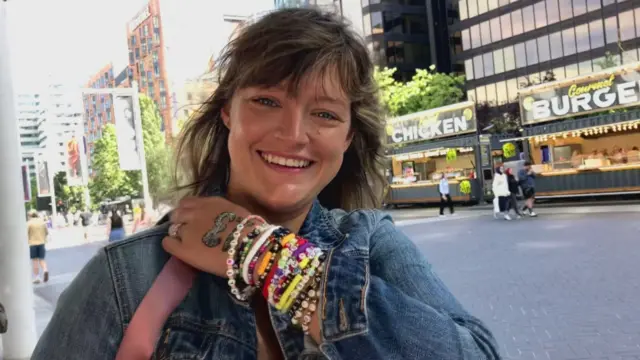 A woman with dozens of friendship bracelets in a denim jacket outside Taylor Swift gig.