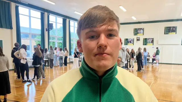 Eoin McMullan wearing a cream/green coloured top looking at the camera smiling in the results hall